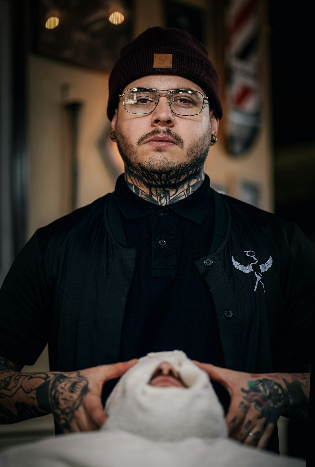 A tattooed barbershop owner in glasses and a beanie, in his shop