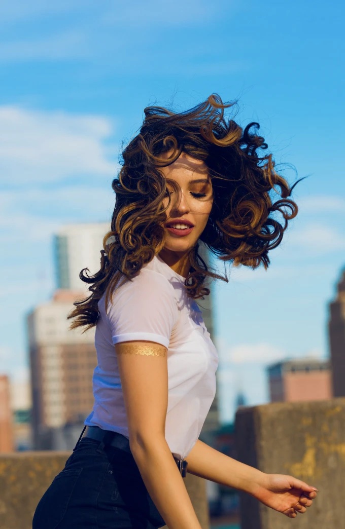 Una donna con i capelli ricci al vento, su un tetto in città